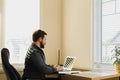 Male broker sitting at desk and using laptop at cabinet.