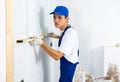 Male builder in blue overalls measures deviations from a given vertical wall using building level