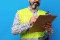 Male builder or handyman in uniform holding clipboard against blue background Royalty Free Stock Photo