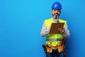 Male builder or handyman in uniform holding clipboard against blue background Royalty Free Stock Photo