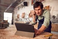 Male Business Owner In Workshop Using Digital Tablet And Making Call On Mobile Phone Royalty Free Stock Photo