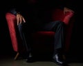 Male businessman in a black suit sitting in red chair, black background, no faces visible, studio shooting