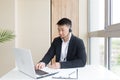 Male businessman conducts online training using a headset and laptop, sitting in a stylish office by the window