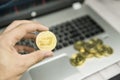 Male businessman hand holding Dash coin on a background of laptop keyboard and pile of golden coins. Virtual money and