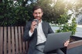 Successful businessman working on laptop and drink coffee at lunchtime sitting on bench near office Royalty Free Stock Photo