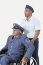 Male cadet assisting senior air force officer in wheelchair over light gray background