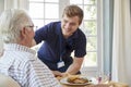 Male care worker serving dinner to a senior man at his home