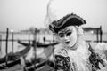 Male carnival goer in traditional costume and mask standing with back to the Grand Canal, gondolas in the background