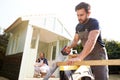 Male Carpenter With Female Apprentice Sawing Wood To Build Outdoor Summerhouse In Garden Royalty Free Stock Photo