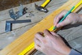 Male carpenter notes with pencil using measuring tape on the board, marks for saw cut. Close up view.