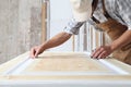 Male carpenter working the wood in carpentry workshop, measuring wooden door with a mesure tape, wearing overall and cap Royalty Free Stock Photo