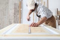 Male carpenter working the wood in carpentry workshop, measuring wooden door with a mesure tape, wearing overall and cap Royalty Free Stock Photo