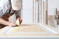 Male carpenter working the wood in carpentry workshop, putting paper masking tape on a wooden door, wearing overall and cap Royalty Free Stock Photo