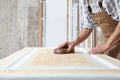 Male carpenter working the wood in carpentry workshop, sanding a wooden door with sandpaper, wearing overall Royalty Free Stock Photo