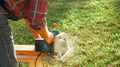 A male carpenter works with a circular saw on the lawn. Close-up view of a working tool. Contrast sunlight with glare scattered in Royalty Free Stock Photo