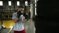 Male, caucasian boxer practicing kicks in black gloces using a puching bag made from car tyres. Old style boxing studio