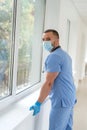 Male caucasian doctor wearing blue medical coat and face mask in modern clinic corridor Royalty Free Stock Photo