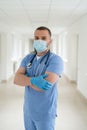 Male caucasian doctor wearing blue medical coat and face mask in modern clinic corridor Royalty Free Stock Photo