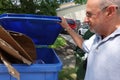 Male Caucasian senior citizen holding open the lid of a recycling trash can and smiling as he looks at the cardboard inside