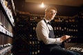 Male cavist examines the bottles with wine and making notes at his notepad