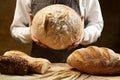 Male chef confectioner in apron hold and show warm round homemade bread over studio background. Whole grain rye bread