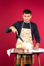 A male chef cuts pumpkin for cooking. Pink background. The concept of combating gender stereotypes
