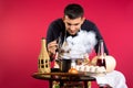 A male chef in the kitchen sniffs cooked dish, steam comes out of the pan. Photo on pink background