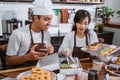 A male chef wearing an apron using a cellphone and a female chef preparing a donut order