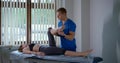 A male chiropractor in a blue t-shirt stretches the legs and knee joints of a young girl, bringing the damage in order