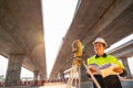 A male civil engineer or surveyor standing holding a blueprint with a happy smile at road construction site, Surveyor equipment. Royalty Free Stock Photo