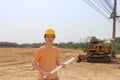 Male civil engineer wear yellow helmet and project drafts while in hand standing on background of front loader engineering