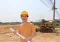 Male civil engineer wear yellow helmet and project drafts while in hand standing on background of front loader engineering