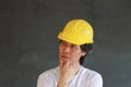 Male civil engineer with yellow helmet and wear white T-shirt on dark grey background. Standing and expressing thoughts