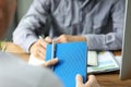 Male clerk holding blue notepad with silver pen talking to colleague