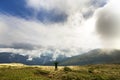 Male climber tourist with raised arms standing on grassy hill slope on green mountains with white puffy clouds and blue sky copy Royalty Free Stock Photo