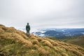 Male climber tourist standing on grassy hill slope on green mountains with white puffy clouds and blue sky copy space background Royalty Free Stock Photo