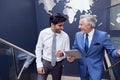 Male Colleagues With Digital Tablet Meeting On Stairs Of Office With World Map In Background