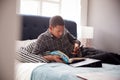 Male College Student Lying On Bed Working In Shared House And Using Mobile Phone Royalty Free Stock Photo