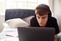 Male College Student Wearing Headphones Lies On Bed In Shared House Working On Laptop Royalty Free Stock Photo