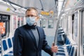 Male commuter poses in empty subway carriage, wears medical mask to prevent infected coronavirus at public metro station, looks Royalty Free Stock Photo