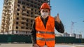 Male construction worker in overalls and in medical mask showing thumbs up on background of house under construction Royalty Free Stock Photo