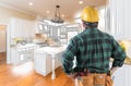 Male Contractor in Hard Hat and Tool Belt Looking At Kitchen Drawing Royalty Free Stock Photo