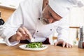 Male cook chef decorating garnishing prepared salad dish on the plate in restaurant commercial kitchen. Royalty Free Stock Photo