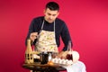 A male cook holding a lid looks into a saucepan. Photo on a pink background. The concept of gender stereotypes