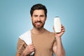 Male cosmetic product advertisement. Positive middle aged man showing blank shampoo bottle, mockup