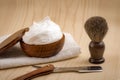 Male cosmetic products and supplies used by men to shave concept with a straight razor, towel, shaving brush and foam on wood Royalty Free Stock Photo