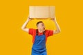 Male courier loader with heavy box over his head screaming. Isolated on yellow background. Copy space, mock up Royalty Free Stock Photo