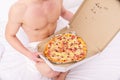 Male courier muscular torso holds pizza. courier delivers gastronomic satisfaction to your bed. Guy naked Royalty Free Stock Photo