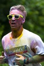 Male covered in paint and wearing lime greem sunglasses running at charity colour paint run. Holding thumbs up.