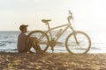 male cyclist is resting sitting on a sandy beach .